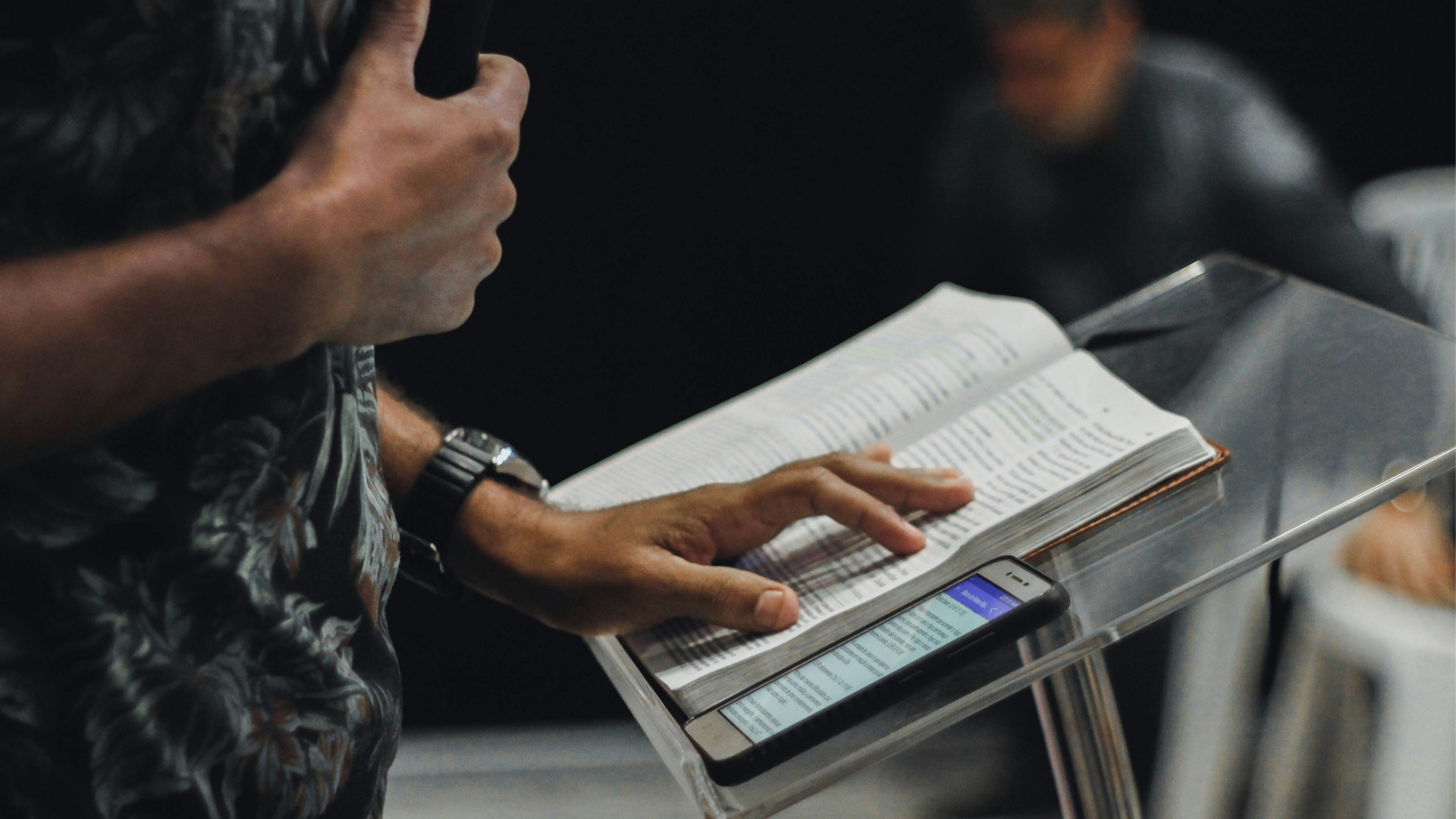 Preacher at the pulpit with an open Bible and phone, midsection view, proclaiming the gospel truth in Africa.