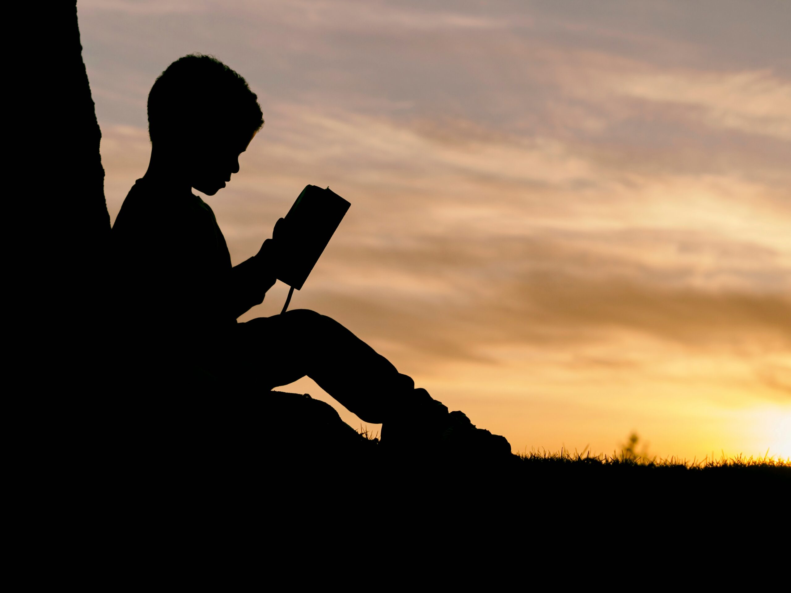 African boy reading the Bible at sunset on a tree stump, symbolizing the light of the Gospel in Africa