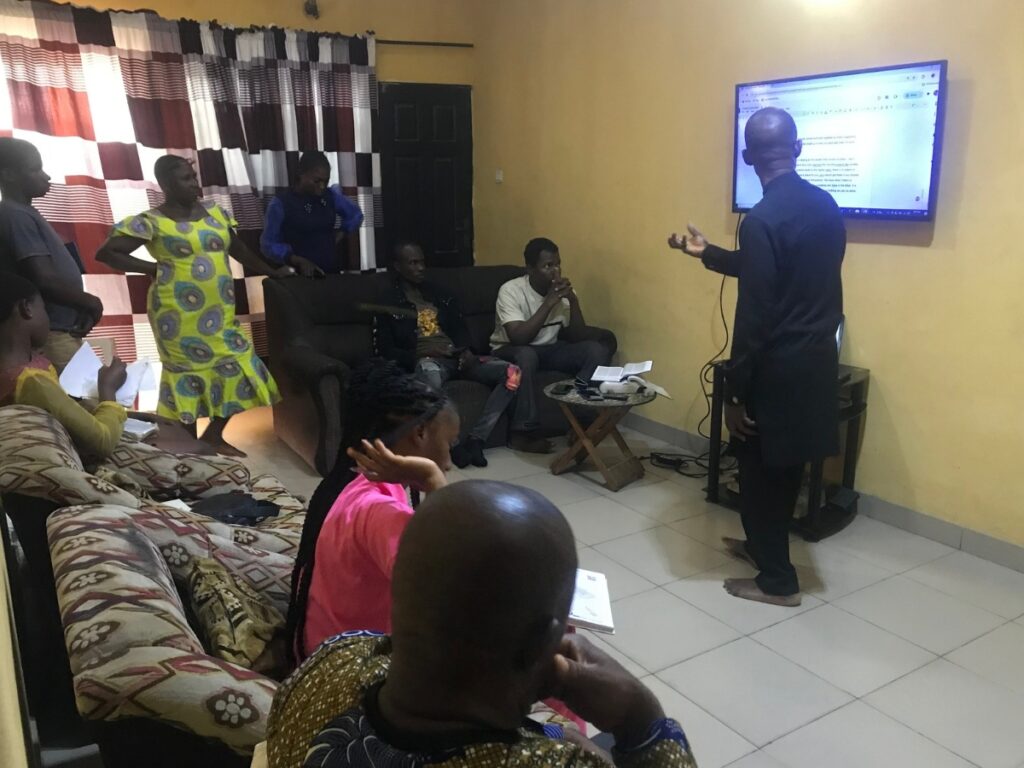 House church fellowship in Nigeria with a teacher leading from a television screen connected to a laptop.