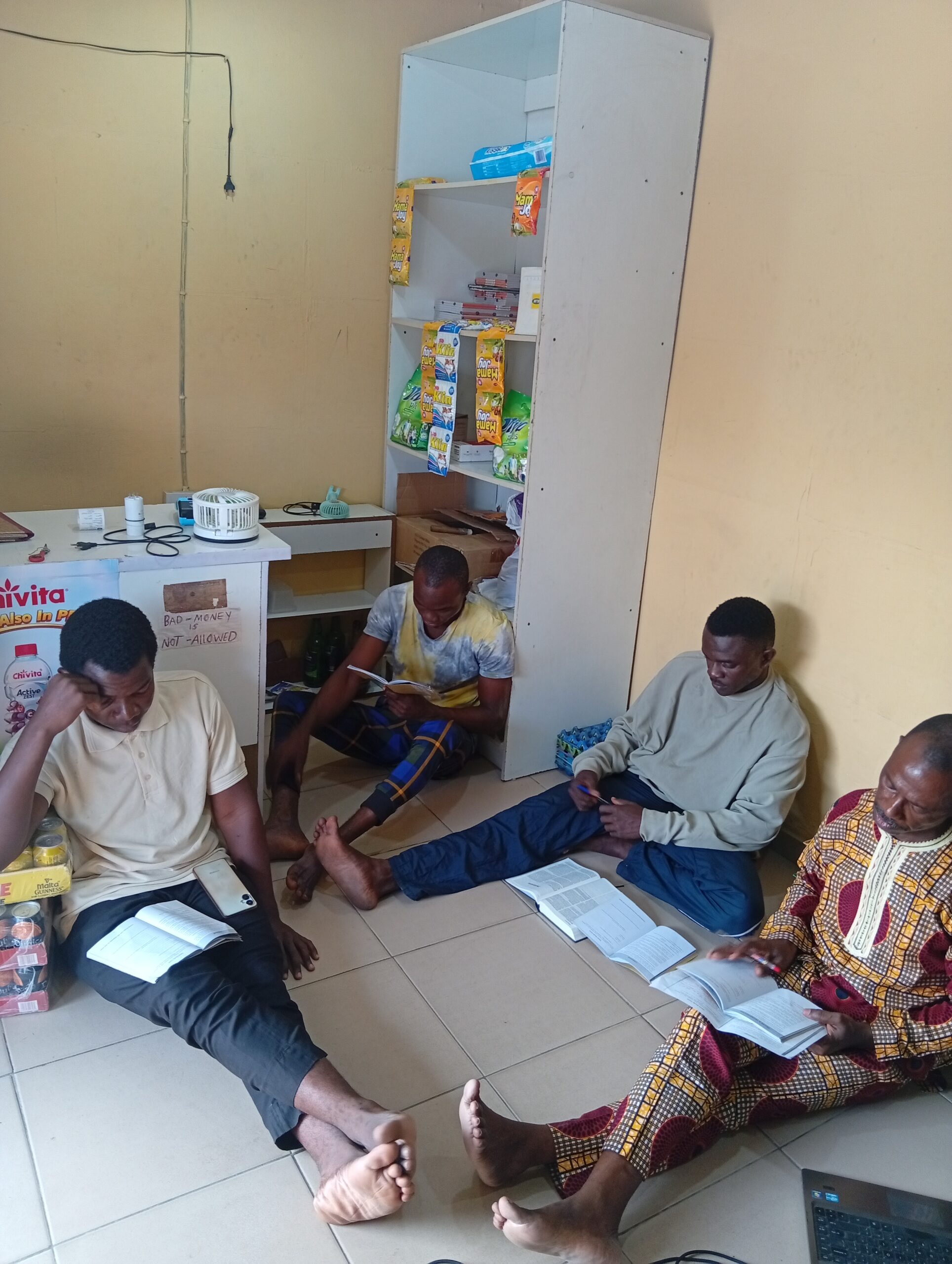 Four young men sitting on the floor in Africa studying the Bible together at a neighborhood shop.
